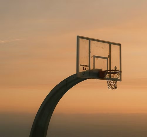 A basketball hoop against an orange evening sky.